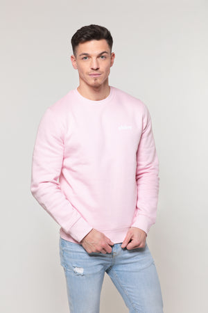Homme mannequin brun, de face, le regard profond et séducteur, pose avec un sweatshirt rose bonbon sur lequel est floqué le mot shiny côté coeur. Le pull semble doux et soyeux.