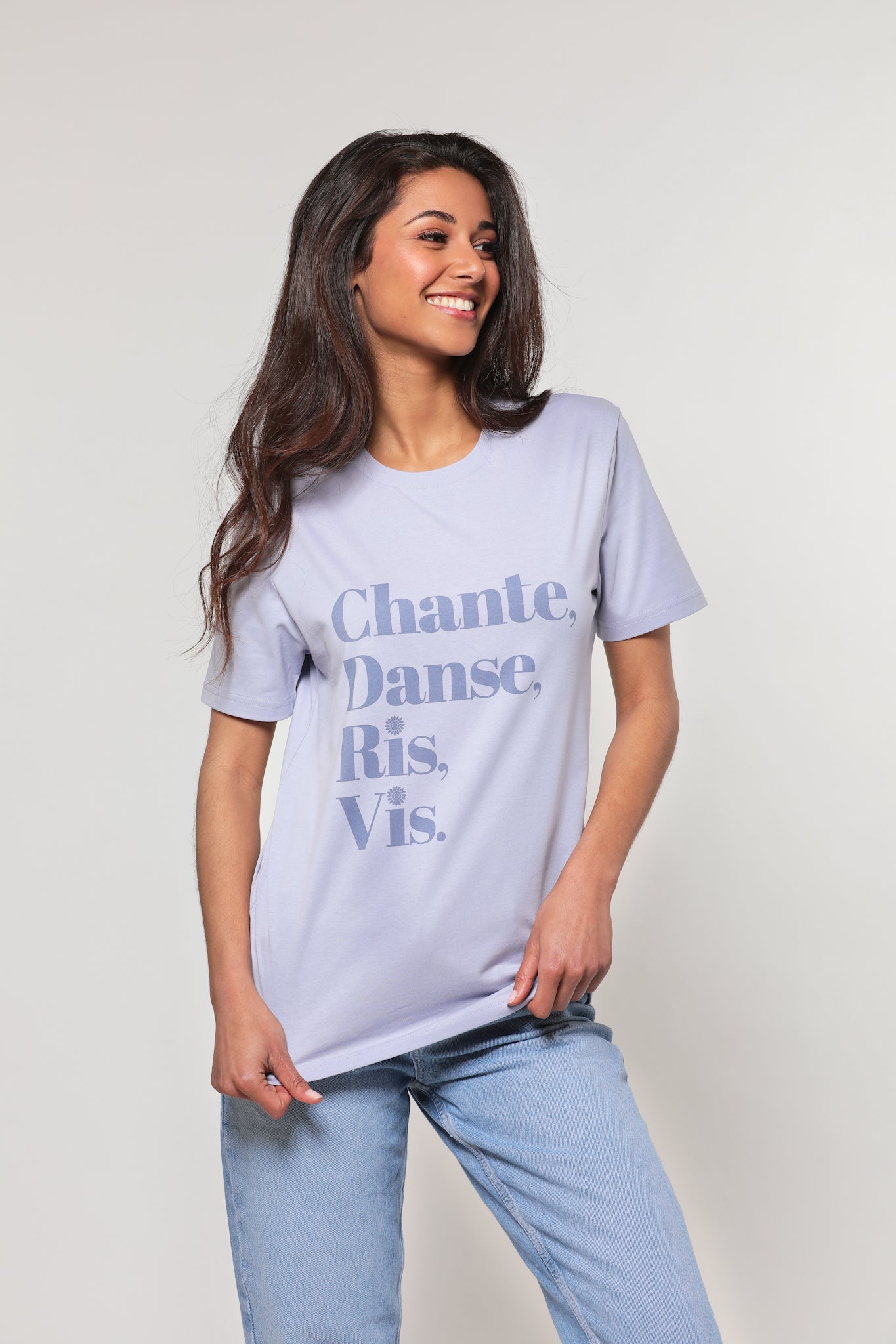 Mannequin femme, brune aux cheveux longs, regard de profil, mains sur son t-shirt, porte un t-shirt lavande avec inscription "Chante, danse, ris, vis" en violet.