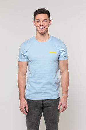 Mannequin homme, jeune, beau et souriant, de face, porte un T-shirt bleu ciel avec inscription du mot sunny en jaune côté coeur. Il porte un jean gris et a du soleil dans les yeux.
