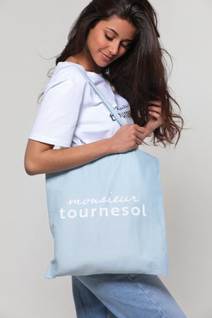 Femme mannequin portant un tote bag, sac de courses, bleu ciel avec le logo de la marque Monsieur Tournesol.